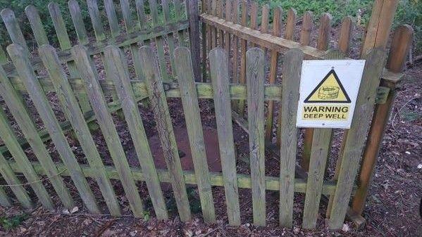 Image shows disused well top enclosed in a triangular picket fence