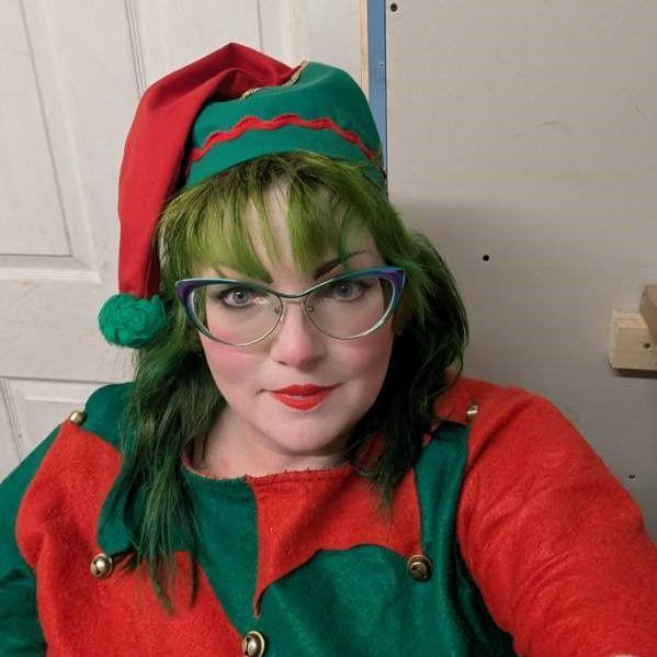 Head-and-shoulders image of Lisa Miller wearing her elf costume. She has purple-rimmed glasses, green hair and a red-and-green bobble hat. Her top is also red and green.