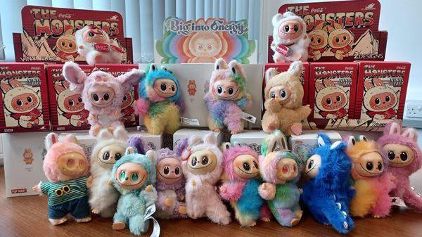 Rows of fake Labubu dolls - cute, multi-coloured monster toys - sitting on a table. Some are still boxed up, while others have been opened.