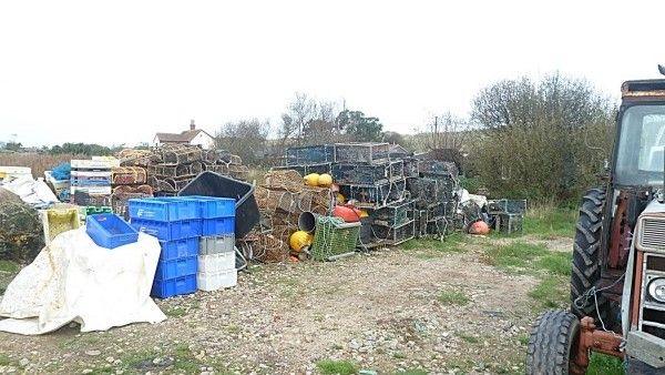 A yard has fishing equipment piled up with a tractor alongside them and with a house and trees in the background.