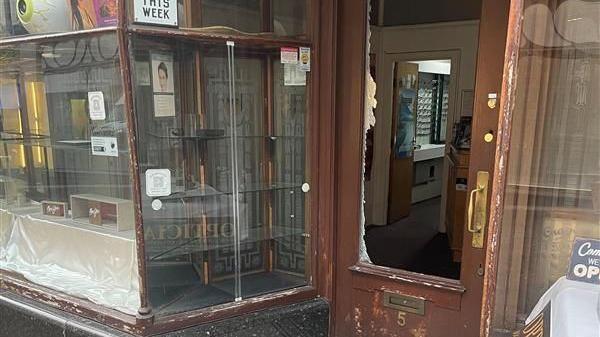 Gray & Bull Opticians on Pelham Street in Nottingham. It has a brown-framed door and windows. The door's glass pane is missing with shards of glass around the edge.
