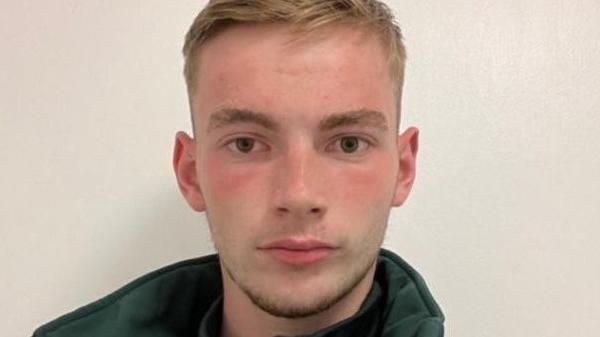 A headshot of Jamie Kadolski looking directly at the camera. He is wearing a green fleece with the collar up. He has short blonde hair.