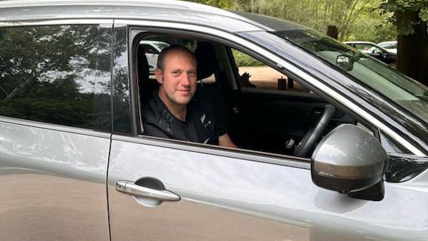 Man sitting in the driver's seat of a silver car.