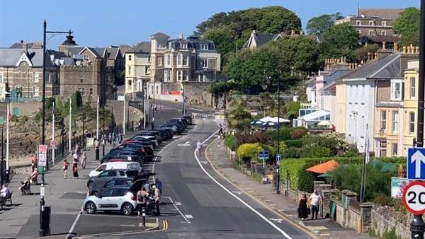 The road along the seafront in Clevedon. There is a line of parked cars facing the sea and buildings either side of the road.