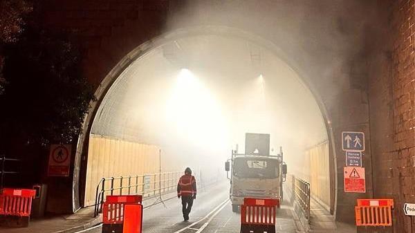 Smoke coming out of the tunnel seen from the outside with orange fencing stopping vehicles from entering and a van parked inside the tunnel.