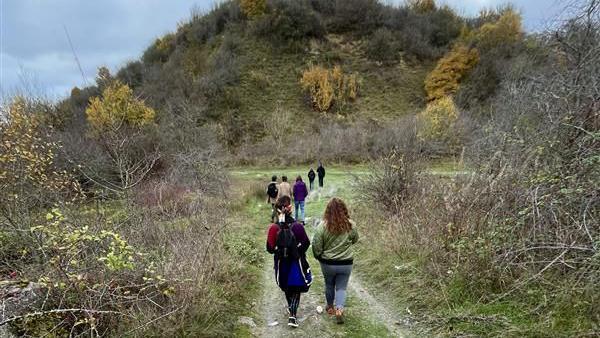 A group of people walking to Waulud's Bank, an ancient site. You can see greenery, bushes and grass, as well as a path. The people are wearing winter coats and are walking away from the camera.