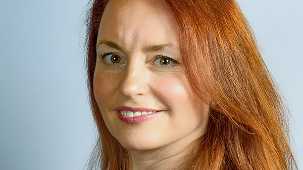 A close up face shot of a red headed woman who is smiling at the camera. 