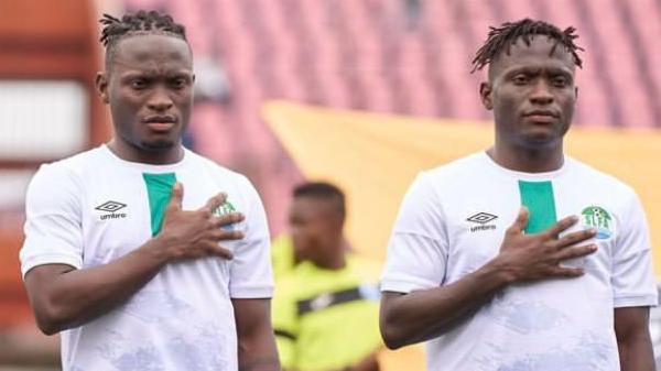 Identical twins Alhassan and Alusine Koroma, wearing white Sierra Leone shirts, both stand with their right hand over their heart during the national anthem