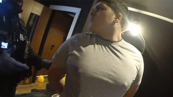 A still image from bodycam footage of Dearnie Jones being arrested. He is wearing a grey t shirt and has his hands behind his back.