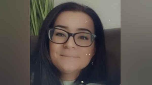 Elise Mason has long black hair and black-framed glasses. She is smiling at the camera and there is a filter on the image.