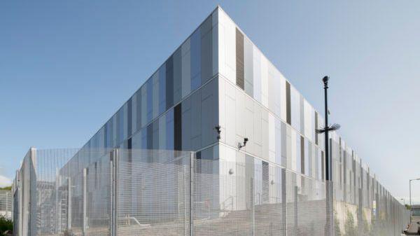 A large silver data centre building, with a mesh fence surrounding it.