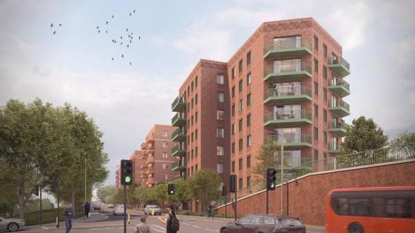 A digital rendering of a modern residential development featuring red brick apartment buildings with green balconies. The buildings are situated along a road with traffic lights, pedestrians, cars, and a red bus. There are trees and greenery surrounding the area.