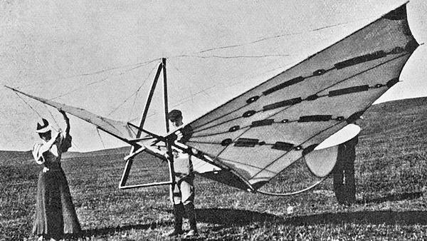 A black and white image of Percy and Ella Pilcher with the Bat Glider, a device with large wings. They are stood in a field holding the Bat Glider.