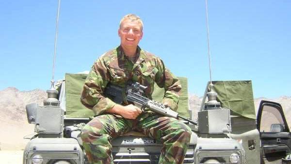 Man in camouflage clothes with a gun, sits on a jeep in the desert. 