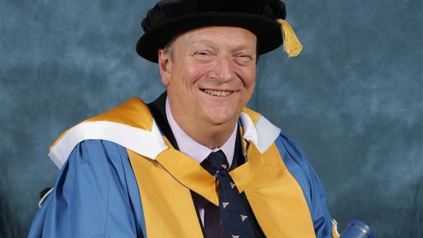Geoff Holt wearing blue, gold and white Bournemouth University gown.