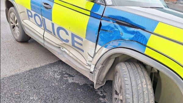 A close up image of a police vehicle shows dents to the front bumper. 