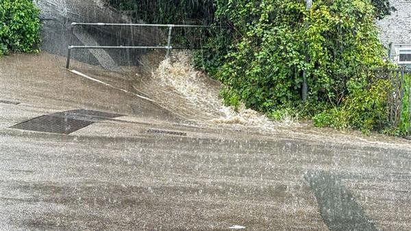 A picture of flooding on a pavement going downhill. The water is flowing fast down the road.