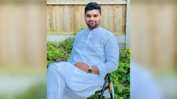 Muhammad Aftab Ahmad, dressed all in white, sits on a chair. A fence and plants are in the background.