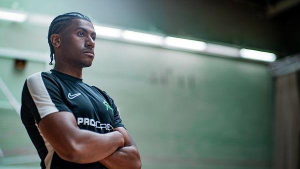 Andre Arissol with short dark hair and beard, wearing a green T-shirt and standing with his arms folded against a green wall.