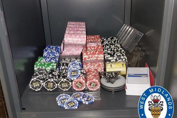 Piles of poker chips of different colours in a safe, along with a triangle "all in" button, on top of a white dealer button, and a pack of cards.
