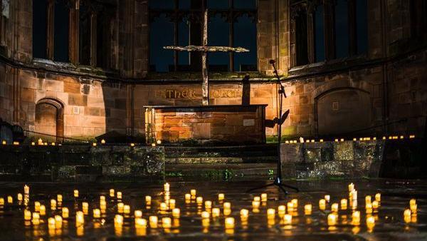 A picture taken from ground level in the cathedral showing small candles on the floor. An old fashioned alter is in the background with a wooden cross behind it.