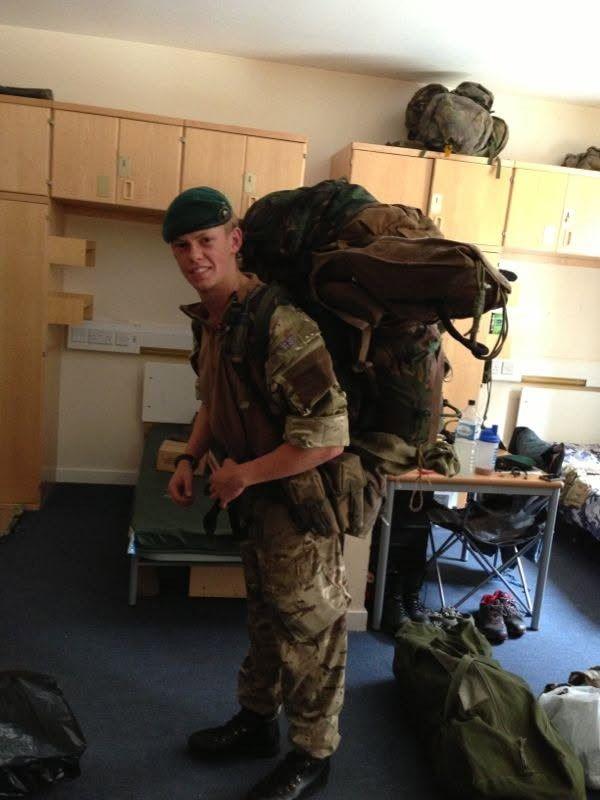 A man in military uniform stands holding a huge rucksack on his bag.