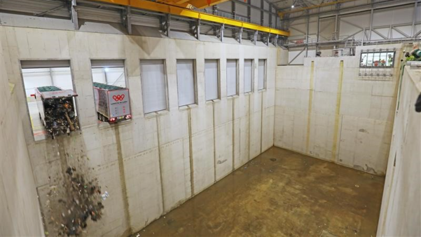 The inside of a large warehouse where trucks can back onto and dump waste into. Two trucks are emptying rubbish into an empty space.
