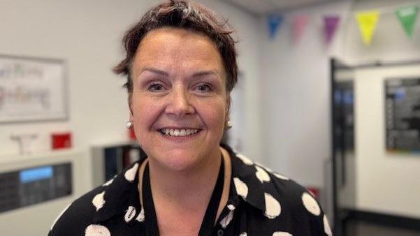 A woman with dark hair and a dark top with large white spots in a room with bunting on the walls