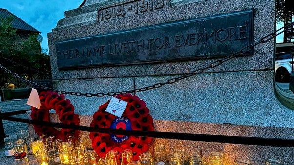 Lit candles in glass jars and two wreathes of poppies laid out at the bottom of the war memorial sculpture