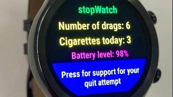 A smartwatch displaying the new app's messages. It shows the words stopWatch in green, with the message - Number of drags: 6, Cigarettes today: 3, Battery level: 98%, Press for support for your quit attempt. 