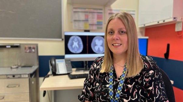 Paediatric neurosurgeon Deborah Ferguson wearing a black patterned dress smiling in a hospital room