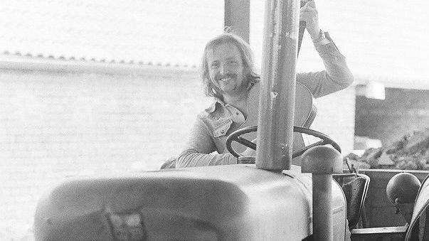 Black and white photograph of Barry Devlin from Horslips - a 1970s man - sits on an old tractor