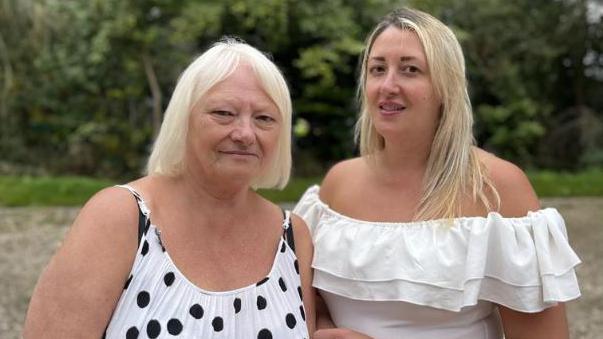 Blonde-woman in a polka dot top accompanied by a younger blonde-haired woman in a ruffled top