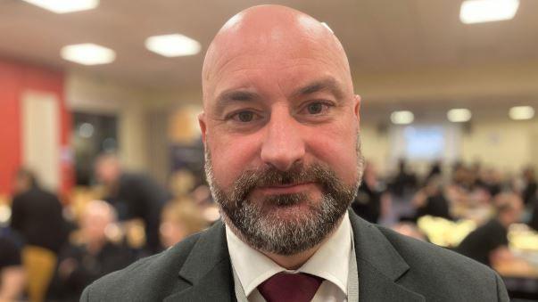 Head and shoulders photograph of Lincolnshire Police and Crime Commissioner Marc Jones. He is bald with a grey and dark brown beard. He is wearing a grey blazer with a white shirt and dark red tie.