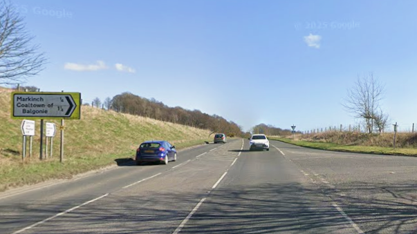 A single carriageway road surrounded by fields on a sunny day. There are three cars on the road