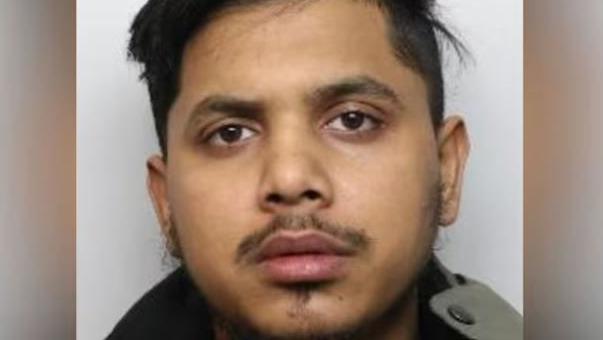 A police mugshot of Jamil Talukder. He has brown eyes, a dark moustache and thin dark hair on his chin and cheeks.