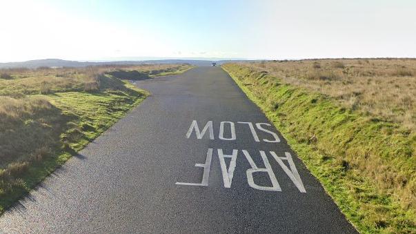 rural road with grass verges and a slow sign painted on the tarmac