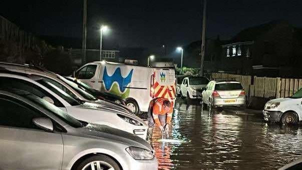 Picture shows flooding in a residential street. Welsh water engineer stands in front of a Welsh Water van working to sort the problem. 