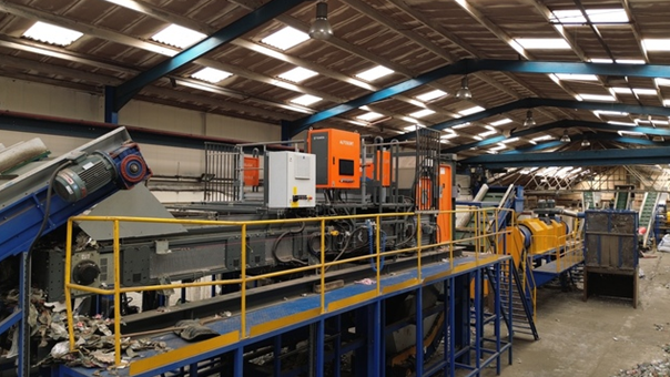 The inside of an industrial building. Various pieces of large machinery can be seen throughout, in the foreground is a blue metal walkway with yellow railing
