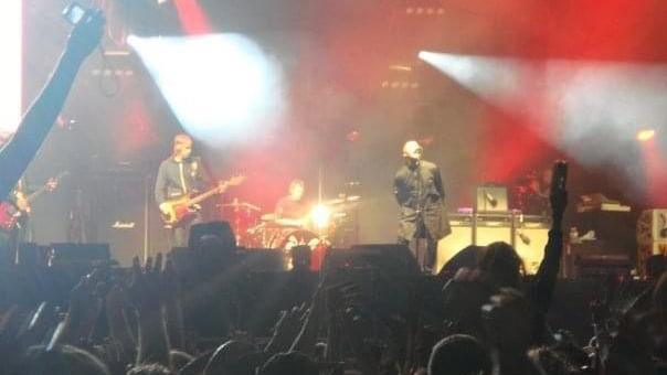 Oasis performs on a stage as fans hold their hands up in the air.