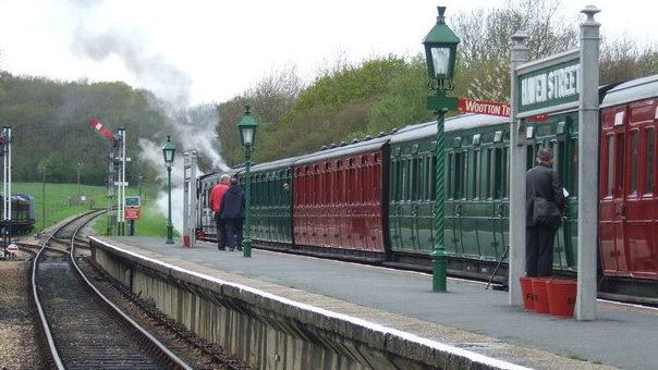 A steam train at Havenstreet station with alternate carriages painted red and green.