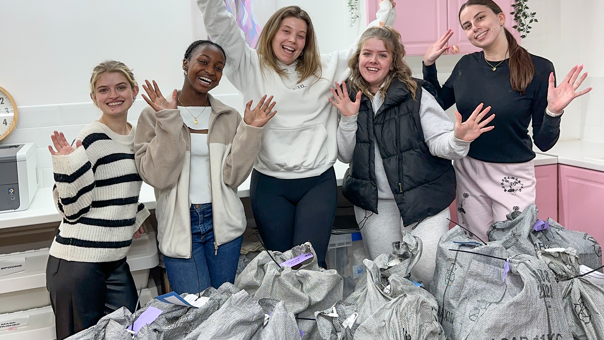 Isobel and four other young women with their hands in the air, behind lots of parcels