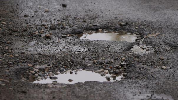 Close up view of two potholes full of water on a black-tarmac road with several stones surrounding them.