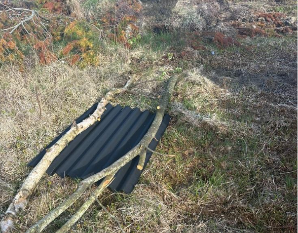 A black metal sheet held down by two long sticks on green grass