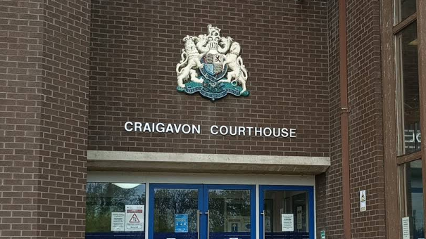 A screen grab of a brown brick building with a silver coat of arms and silver writing that says 'Craigavon Courthouse'. 