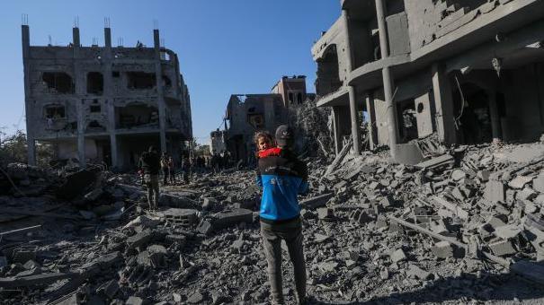 A Palestinian father carries his daughter next to a destroyed house in Al Maghazi refugee camp, central Gaza Strip on 03 January 2025.