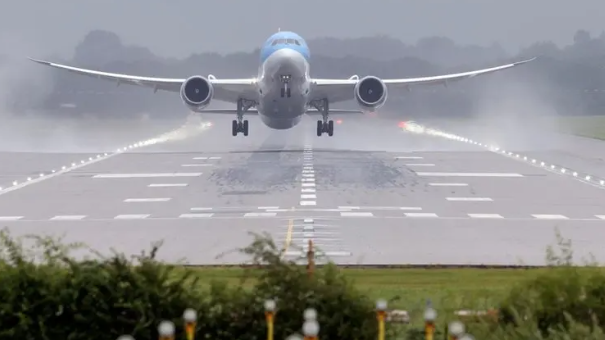 A plane landing at Gatwick Airport. The plane is very close to the ground on the runway, which has water sprayed up each side due to rainy conditions. The plane is white and pale blue. 