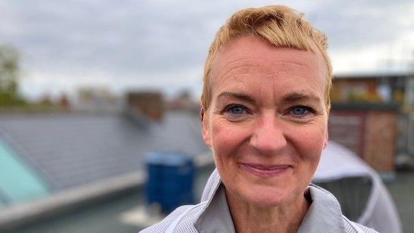 Woman with short blonde hair smiles at the camera while standing on the roof at the Civic Centre.