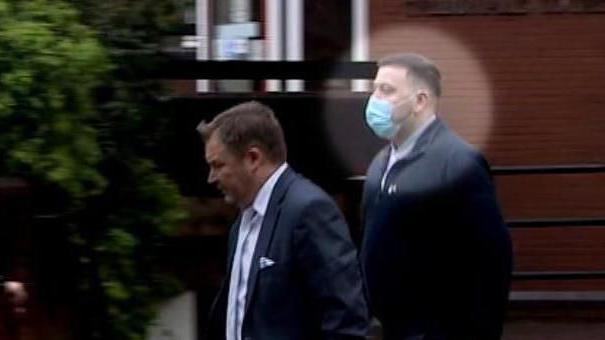 Paul Hanson, wearing a facemask and a black suit outside a red brick court building