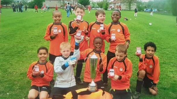 A youth team at Cray Wanderers celebrate a trophy, with a young Marc Guehi holding the trophy in the centre